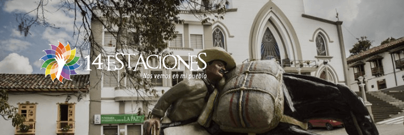 Un colorido logotipo de 14 Estaciones se superpone a una estatua de un hombre con una mula frente a edificios de estilo colonial y la iglesia de Apía, Risaralda, con el texto Nos vemos en mi pueblo. Al fondo se ven árboles y un cielo nublado.