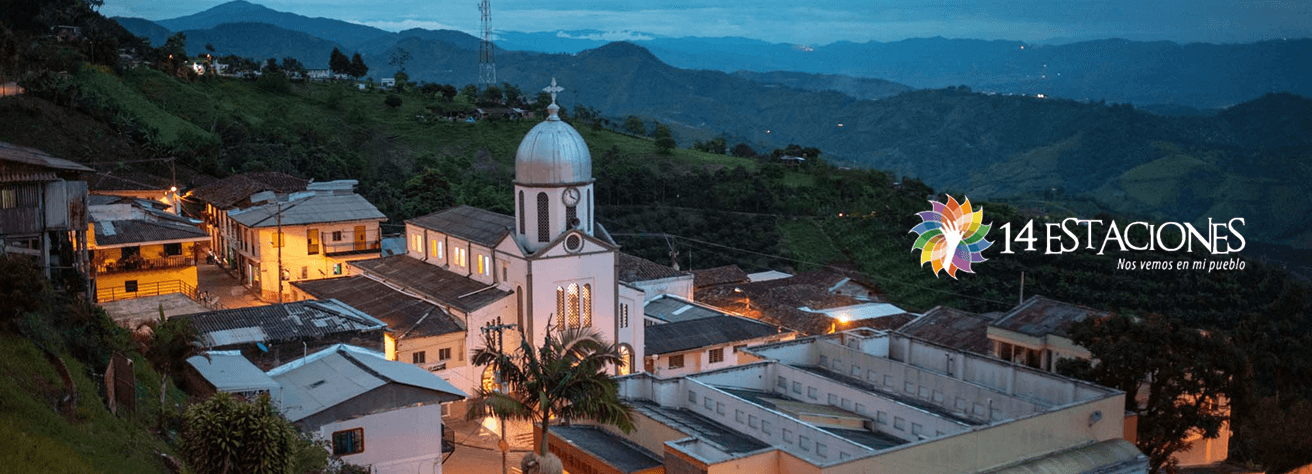 Una pequeña ciudad con edificios blancos y una iglesia central con cúpula, enclavada en verdes colinas al atardecer, evoca el encanto de las estaciones Balboa. El logotipo "14 Estaciones" con un colorido diseño floral aparece a la derecha.