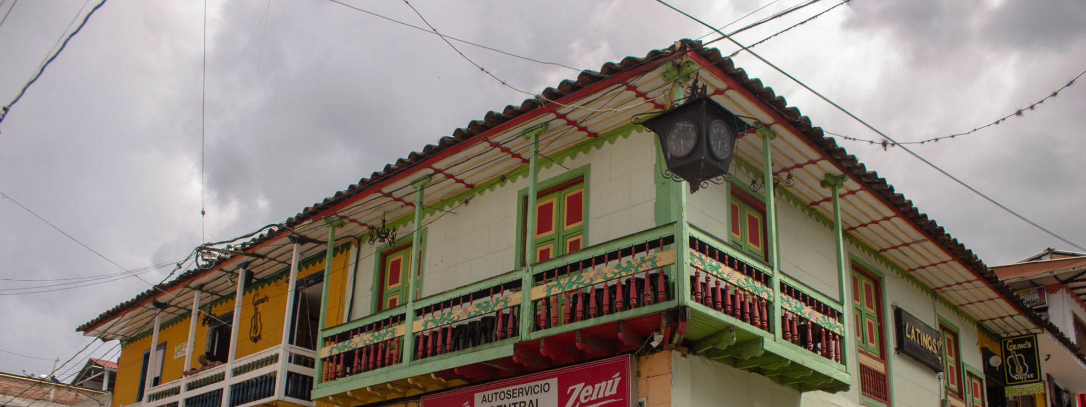 Cerca de la Biblioteca Pública Municipal, bajo un cielo nublado, se levanta un colorido edificio con adornos de madera y balcones rojos, verdes y blancos, sobre el que se entrecruzan cables eléctricos.