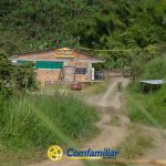 Un camino de tierra conduce a un edificio de ladrillo rotulado ARABEL, rodeado de frondosa vegetación y árboles. Un coche rojo está aparcado fuera, sugiriendo la Biblioteca Municipal. El logotipo de Comfamiliar Risaralda aparece en la parte inferior de la imagen.