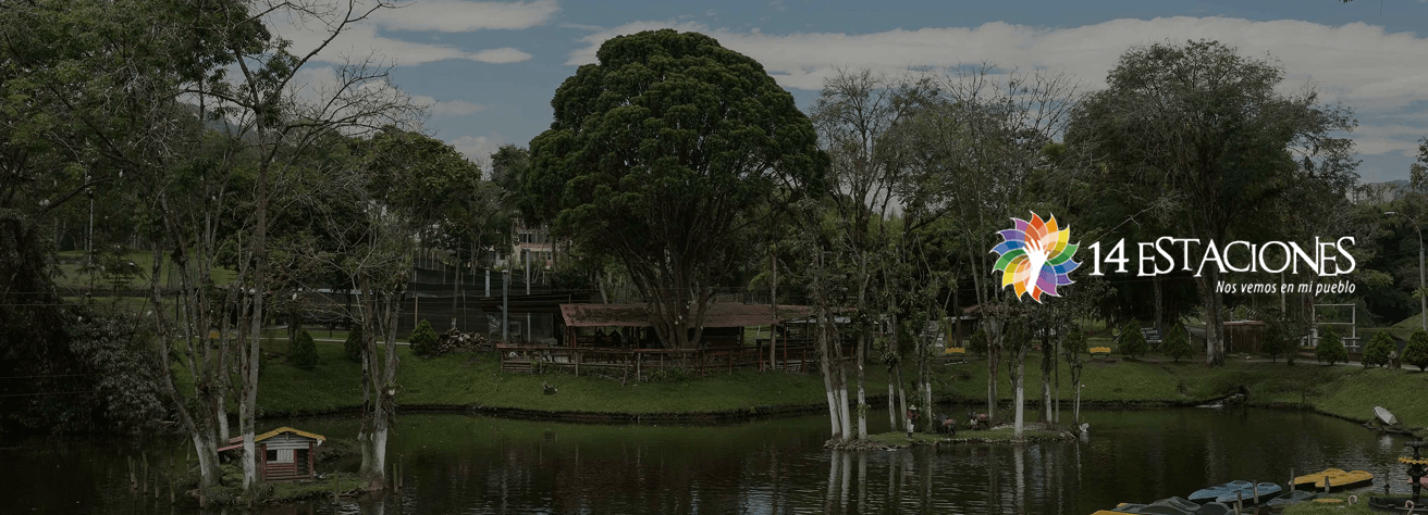 Un parque escénico en Dosquebradas, Risaralda cuenta con árboles altos, un estanque con pequeños muelles y botes, y un edificio rústico de madera. El logotipo de 14 Estaciones y el lema "Nos vemos en mi pueblo" aparecen a la derecha.