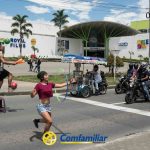 Dos artistas callejeros hacen malabares en un paso de peatones de Dosquebradas; uno hace equilibrios sobre un taburete con un balón de fútbol, mientras el otro hace malabares con anillas. En la calle se ve un logotipo de Comfamiliar, y la gente mira desde la acera.
