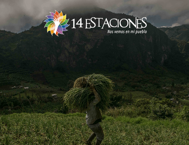 Una persona lleva un gran haz de hierba a la espalda en un campo frondoso y verde con montañas al fondo. El logotipo 14 Estaciones Guática y el texto Nos vemos en mi pueblo aparecen en la parte superior de la imagen.
