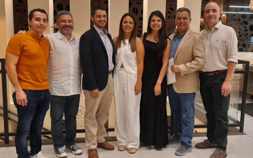 Siete personas están de pie, una al lado de la otra, sonriendo a la cámara. Vestidos con elegantes atuendos informales, representan el espíritu del evento MIND OF A SURGEON (MOAS) de la AAGL. El fondo presenta una decoración moderna y una iluminación cálida.