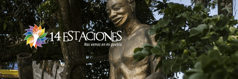 Una estatua dorada de una persona sonriente se alza entre verdes árboles en Risaralda. El texto superpuesto dice 14 Estaciones. Nos vemos en mi pueblo junto a un colorido logotipo en forma de flor a la izquierda.