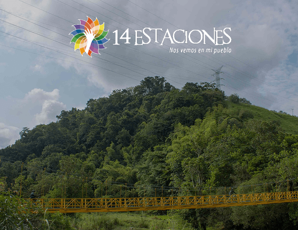 Un puente colgante de color amarillo brillante atraviesa un exuberante paisaje verde con una colina y árboles bajo un cielo nublado. En la parte superior, el colorido logotipo y el texto 14 Estaciones - Nos vemos en mi pueblo destacan la ruta de estaciones Marsella.