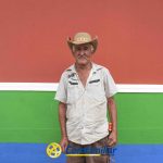 Hugo Ángel Jaramillo, un hombre mayor con sombrero vaquero y camisa de mangas cortas, ante una colorida pared con secciones rojas, verdes y azules, cerca de la Biblioteca Pública. El logotipo de Confamiliar aparece en la parte inferior de la imagen.