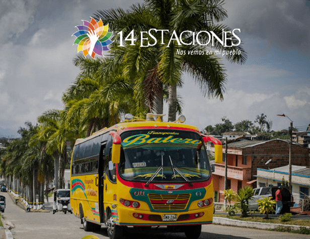 Un colorido autobús Batero recorre una calle bordeada de palmeras en Quinchía, Risaralda, captando el encanto tropical de este pequeño pueblo. Arriba, el logotipo de 14 Estaciones y "Nos vemos en mi pueblo".