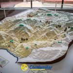 En una vitrina de la Biblioteca Pública se expone un modelo topográfico en 3D de una región montañosa. En la vitrina se ven el logotipo y el texto Comfamiliar, y en una esquina aparece una leyenda con la etiqueta QUINCHÍA.