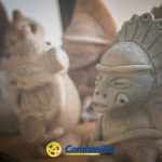 Varias figurillas de arcilla con diseños intrincados, que muestran el arte precolombino, se exponen muy juntas en la Biblioteca Pública Municipal. En la parte inferior de la imagen puede verse el logotipo de Comfamiliar Huila.
