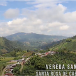 Un paisaje montañoso verde y exuberante con casas dispersas bajo un cielo parcialmente nublado. El texto en la imagen dice: "Vereda Santa Bárbara, Santa Rosa de Cabal - Risaralda". Cerca de la Biblioteca Pública Jaime Fernández Botero.