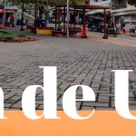 Una plaza pública en Belén de Umbría, cerca de la Biblioteca Pública Municipal, con bancos, árboles, gente, una escultura de un jeep verde brillante y grandes letras amarillas de BELÉN al fondo.