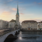 Un puente de piedra cruza un río en dirección a edificios históricos y una iglesia con una alta torre del reloj en Zúrich, Suiza, bajo un suave cielo al atardecer.