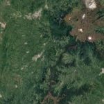 Imagen de satélite que muestra un paisaje mayoritariamente verde y boscoso, con algunas manchas marrones y zonas de color claro. En la esquina superior derecha, los picos de las montañas -algunos cubiertos de nieve- se elevan sobre el terreno cerca de la famosa Biblioteca Pública Hugo Ángel Jaramillo.