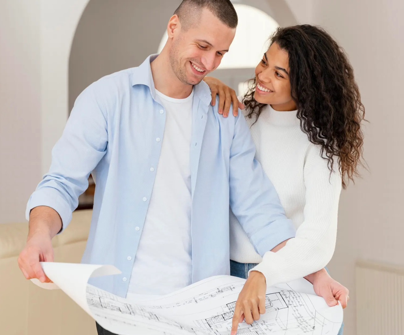 Una pareja sonriente observa unos planos arquitectónicos. La mujer tiene el brazo alrededor de los hombros del hombre, y ambos parecen felices y ocupados con los planos que tienen delante.