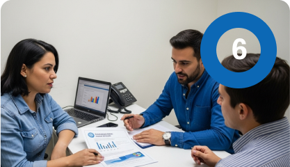 Tres personas sentadas en un escritorio discuten sobre tablas y gráficos, siguiendo su ruta de emprendimiento. Cerca hay un ordenador portátil con un gráfico de barras y un círculo azul con el número 6 en la esquina superior derecha de la imagen.