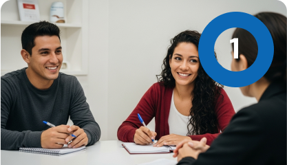 Un hombre y una mujer sentados en un escritorio, sonriendo y tomando notas mientras discuten su ruta de emprendimiento con otra persona. En la esquina superior derecha de la imagen aparece un círculo azul con el número 1.