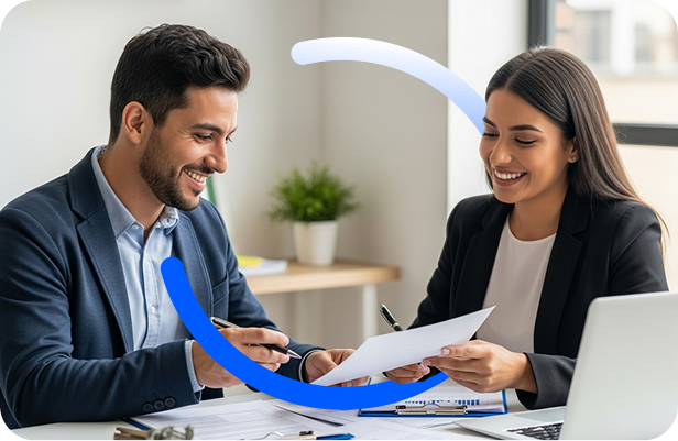 Un hombre y una mujer en traje de negocios se sientan en un escritorio, sonriendo y discutiendo juntos documentos de Gestión Empresarial en una oficina luminosa y moderna. Al fondo se ve una maceta y una gran ventana.