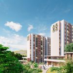 Modernos edificios de apartamentos con fachadas rojas y blancas se elevan sobre zonas verdes ajardinadas, árboles y senderos bajo un cielo azul brillante con nubes dispersas. La gente pasea y se reúne alrededor de los edificios.