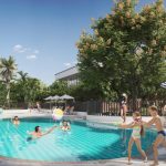 En Montebonito Apartamentos, los niños juegan con una pelota de playa en la piscina mientras los adultos descansan cerca. La gente se relaja bajo sombrillas a rayas y las palmeras rodean la zona en un día soleado.