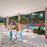 Una familia de tres miembros baila junta bajo un patio cubierto con mesas y sillas blancas en el Parque Arboleda, cerca de una zona de piscina con montañas y palmeras de fondo, creando un ambiente alegre.