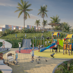 Los niños juegan en coloridos juegos infantiles mientras los adultos supervisan y se relajan cerca, en Villabosque Nativo, un parque con palmeras, exuberante vegetación y modernos edificios de fondo bajo un cielo despejado.