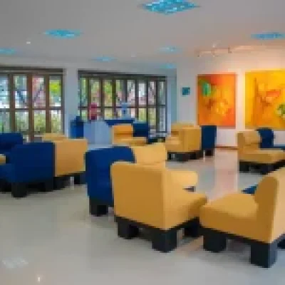 El moderno salón del Auditorio Colibrí cuenta con sillones amarillos y azules dispuestos en pequeños grupos, coloridos cuadros abstractos en las paredes, grandes ventanales que dejan entrar la luz natural y un ambiente limpio y luminoso.