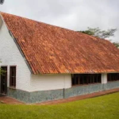 El Auditorio Golondrina es un edificio blanco con un empinado tejado de tejas marrón rojizo y varias ventanas, situado sobre un césped verde con árboles al fondo bajo un cielo nublado.