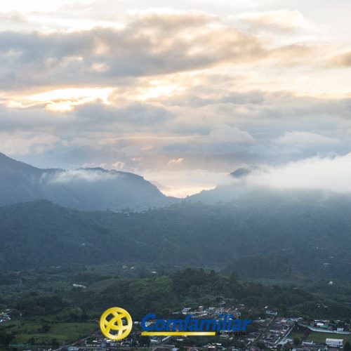 Una vista panorámica de montañas y valles al amanecer o al atardecer, con nubes y niebla sobre el paisaje. El logotipo de la Biblioteca Pública Municipal, obra de Danilo Calamata, aparece en la parte inferior central de la imagen.