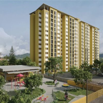 El alto y amarillo edificio de apartamentos Torres del Bosque se alza detrás de un aparcamiento y un pequeño parque infantil con toboganes y columpios, rodeado de árboles y vegetación bajo un cielo parcialmente nublado.