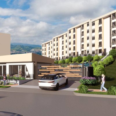 Un moderno complejo de apartamentos de varias plantas se asienta en la ladera de una colina de las Serranías, con una entrada reservada, caseta de seguridad, zonas verdes y gente paseando por la acera. Las montañas sirven de telón de fondo.
