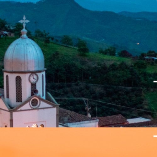 Una pequeña ciudad con una iglesia y una cúpula blancas está iluminada por luces cálidas al atardecer, rodeada de verdes colinas y montañas. Las palabras "Balboa" y "Biblioteca Pública Municipal Juan XXIII" están escritas en grandes letras blancas sobre la imagen.