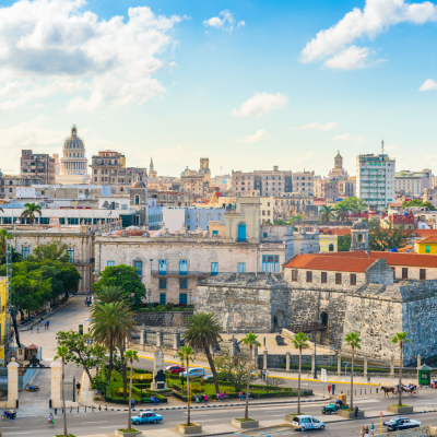 Un vibrante paisaje urbano de La Habana, Cuba, con coloridos edificios coloniales, el histórico Castillo de la Real Fuerza, palmeras y coches clásicos, perfecto para los viajeros que buscan un plan bajo de bajo coste en Cuba bajo un cielo parcialmente nublado.