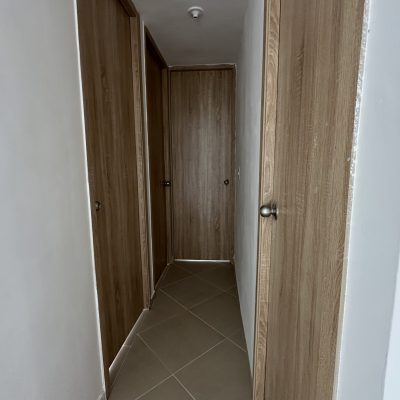 El estrecho vestíbulo del Mirador Campestre presenta puertas de madera de color marrón claro a ambos lados y al final, complementadas con paredes blancas y suelo de baldosas beige.