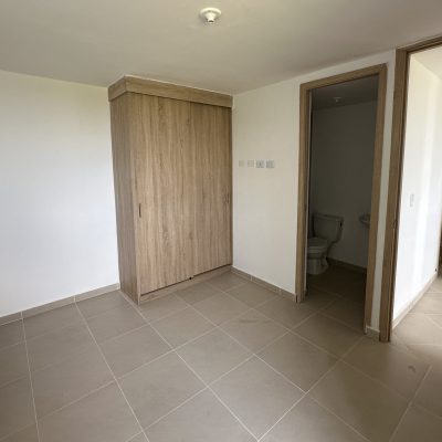 Pequeña habitación sin amueblar en Mirador Campestre con suelos de baldosas beige, armario de madera, paredes blancas y dos puertas abiertas que dan a un cuarto de baño y a un pasillo.