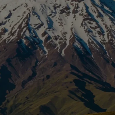 El Nevado del Ruiz, de cumbres nevadas y laderas escarpadas, se alza contra un cielo azul despejado, con verdes colinas más bajas en primer plano; perfecto para una pasadía explorando su belleza y relajándose en los termales cercanos.