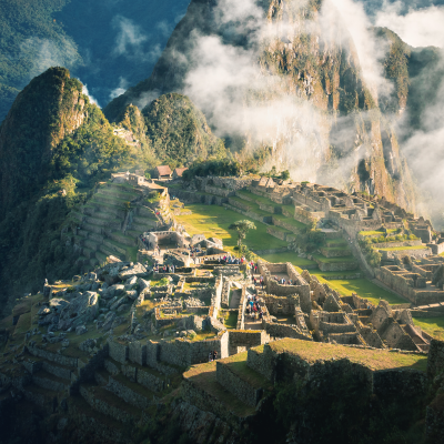 Las antiguas ruinas de piedra de Machu Picchu se asientan en lo alto de una montaña verde y exuberante, rodeada de picos escarpados y nubes que se deslizan por los valles a la luz de la madrugada.